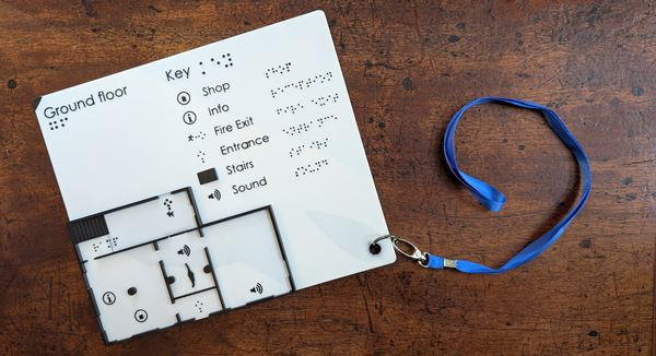 photo of a plastic board with a building plan in relief, labelled in braille.
